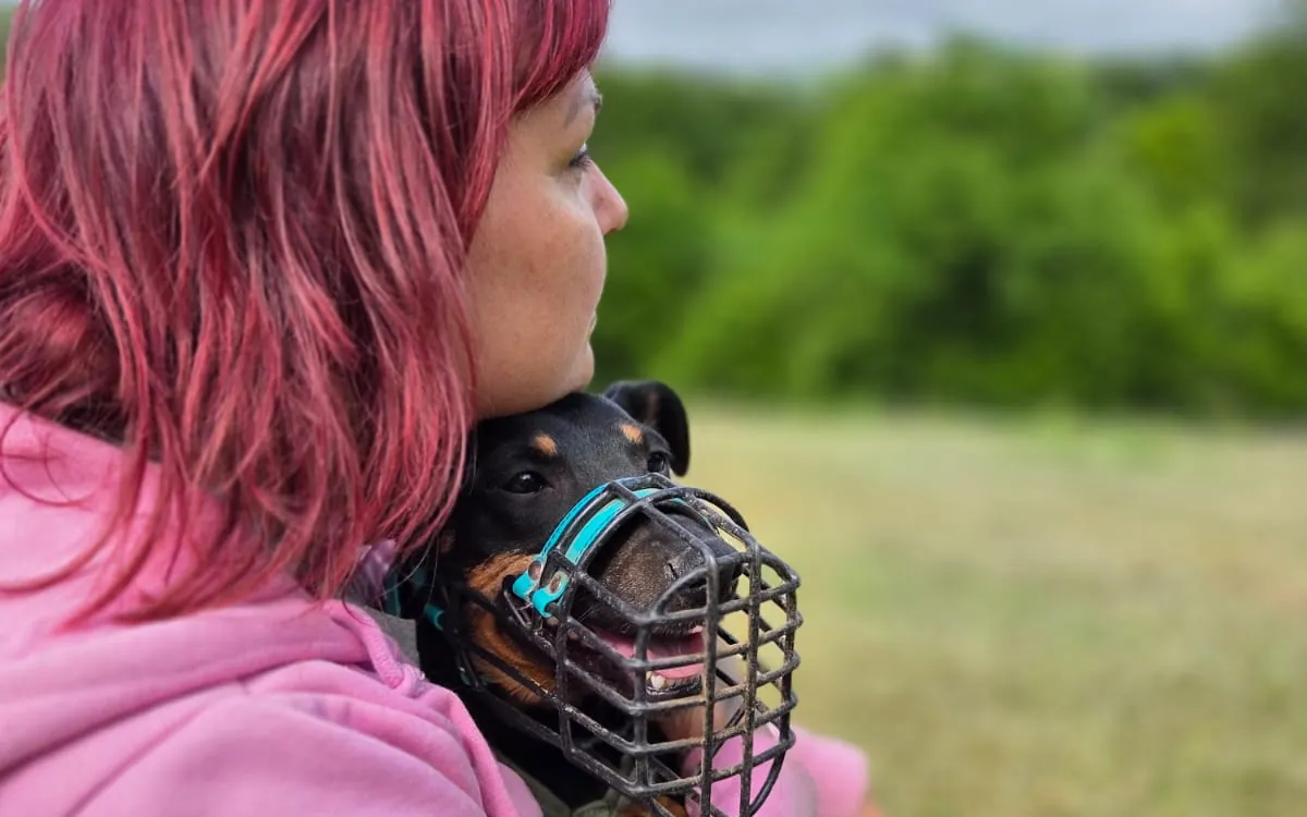 Eine Frau im Profil h&auml;lt einen Hund im Arm, der einen Drahtmaulkorb tr&auml;gt